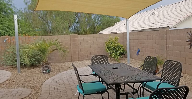 Vacation rental backyard image showing a yellow shade sail protecting and shading a patio dining set.